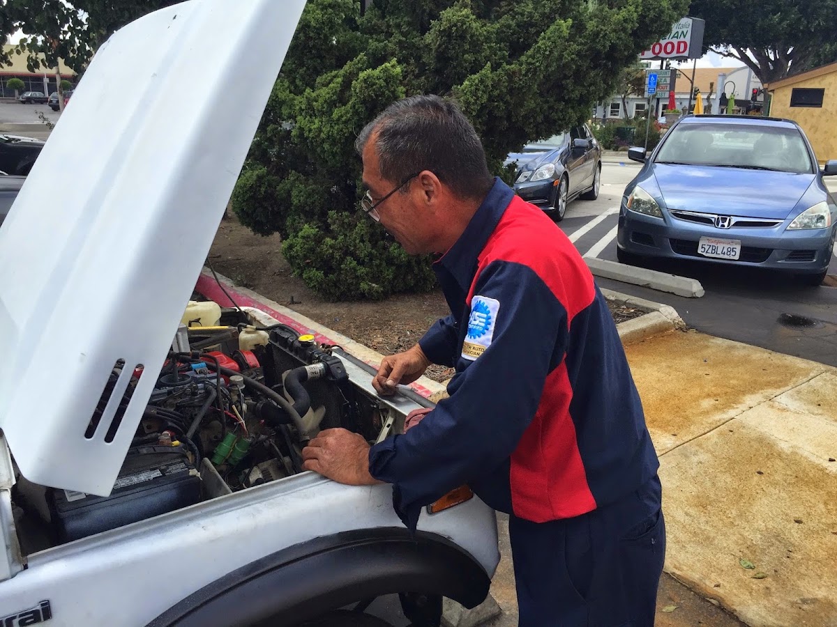 A Galaxy Automotive technician in a red and blue shirt working under the hood of a white car
